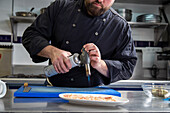 Crop bearded man in black uniform using gas burner to cook slices of pork on plate during work in restaurant