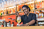 Smiling African American female bartender mixing cold cocktail placed on counter in bar