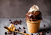 Delicious sweet chocolate ice cream with glaze and cream served with cocoa powder near spoon and chocolate drops in waffle cone
