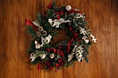 Stylish Christmas wreath with coniferous twigs and decorative elements hanging on wooden wall in daylight