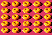 Draufsicht auf viele Donuts mit gelber Hülle und bunten Kugeln auf rosa Hintergrund