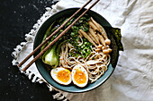 Blick von oben auf eine Keramikschüssel mit köstlichen Ramen und Essstäbchen auf einem mit weißer Tischdecke bedeckten Tisch