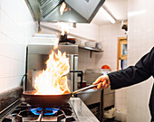 Seitenansicht eines gesichtslosen Kochs, der ein Gericht in einer Bratpfanne auf dem Herd zubereitet, während er in der Küche eines Restaurants arbeitet