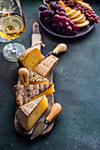 From above cheese variety on the wooden cutting board, fruit plate and wine glasses