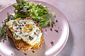 Spiegelei auf Brioche, serviert auf einem Teller mit frischem Salat zum appetitlichen Frühstück auf rosa Hintergrund