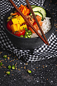 High angle of Asian poke with salmon and rice with assorted vegetables served in bowl on table with chopsticks in restaurant
