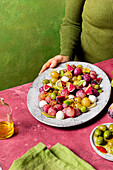 Cropped unrecognizable cook holding plate with fresh ripe grapes, olives, figs and mozzarella seasonal christmas salad placed on plate on green tabletop background
