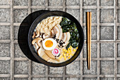 Top view of appetizing Japanese ramen with mushrooms and egg served on paved sidewalk with chopsticks on sunny street in city