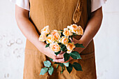 Anonymous adult Hispanic female florist in apron arranging bouquet of assorted gentle fresh flowers against white background
