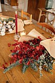 Festlicher, stilvoller, dekorativer Weihnachtsstrauß mit Eukalyptuszweigen und leuchtend roten Zweigen mit Beeren auf einem Holztisch mit Kerzen im Raum von oben