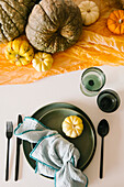 Top view of glasses and plate with napkin served on table decorated with assorted pumpkins during Halloween celebration