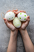 From above cropped unrecognizable kid with hands full with stripped and dot's eggs on grey concrete background