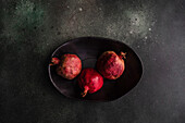 From above organic whole pomegranate fruits with its seeds on black stone background