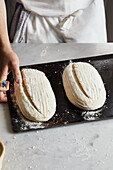 Anonymous baker in apron with blade scoring raw sourdough loaf on table while preparing bread in kitchen