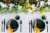 Draufsicht auf Teller und Schüssel mit Besteck und Serviette, die auf einem mit zarten frischen weißen und gelben Blumen geschmückten Tisch serviert werden