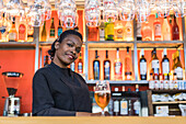Cheerful black female barkeeper serving glass of refreshing beer in bar looking at camera