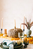 Kreative Tischdekoration mit verschiedenen Kürbissen, brennenden Kerzen und Vasen mit trockenen Pflanzen in der Nähe von Keramiktellern und Gläsern während eines Halloween-Dinners