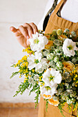 Anonymous adult Hispanic female florist with dark hair in apron arranging bouquet of assorted gentle fresh flowers against white background