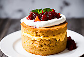 Appetizing baked biscuit cake with cream and decorated with raspberries in syrup with mint leaves on plate