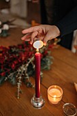 Crop unrecognizable woman lightning candle placed on wooden table with Christmas decorations in room