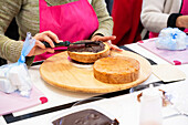 Crop anonymous female in apron putting chocolate cream on biscuit piece while working in professional bakery