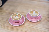 Mugs of hot coffee with creative latte art served on plate with teaspoon on wooden table in modern light coffee house