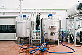 Side view of male engineer examining stainless steel tank with hoses in brewery with wet floor