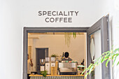Through doorway of unrecognizable barista standing at counter with professional equipment and coffee grinders in modern cafeteria during workday