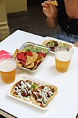 From above of appetizing nachos with salad and tacos with sauce on plates served with glasses of beer in restaurant