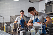 Focused young Hispanic male chef with dark hair in casual clothes and apron adding dry broth into saucepan while cooking in restaurant kitchen with modern appliances