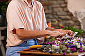 Cropped unrecognizable female florist making flower wreath with ribbon bow while working in floral shop