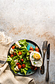 Gesundes Mittagessen mit frischem Bio-Gemüsesalat, Spiegelei und Würstchen, serviert auf einem Betontisch