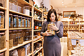 Calm pregnant woman with brown hair in casual dress standing with glass jar with cereal in hands while choosing products in eco friendly store