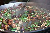 Closeup of unrecognizable cook stirring appetizing dish with chicken and green and white beans in paella pan
