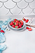 From above bowl of ripe strawberries placed on counter near fresh white flowers and opened book in daytime at home