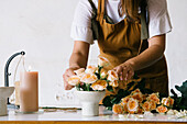 Anonymous adult Hispanic female florist with dark hair in apron arranging bouquet of assorted gentle fresh flowers against white background