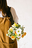 Anonymous adult Hispanic female florist with dark hair in apron arranging bouquet of assorted gentle fresh flowers against white background