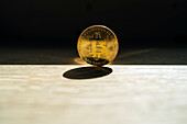 Metal coin with ornament and letter representing cryptocurrency symbol on desk with shade on dark background