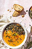 Top view of appetizing homemade pumpkin purees with seeds and herbs in bowls placed on table near crispy bread slices in kitchen