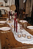 Weißes Tischtuch und Teller auf einem festlich gedeckten Tisch mit brennenden Kerzen und trockenen Baumzweigen
