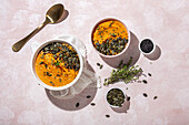 From above of white ceramic bowls with delicious healthy pumpkin cream soup with seeds and rosemary placed on table in kitchen