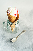Glass jar with waffle cone filled with cherry ice cream on concrete table