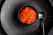 From above red fresh trout fish caviar served in a bowl on concrete table background