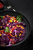 Homemade Purple Cabbage Salad with Corn, Carrots, Pomegranate and Spinach on dark background. Vegan food concept. Healthy food