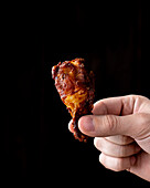 Crop anonymous person demonstrating tasty fried chicken wing on black background in studio