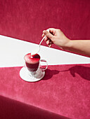 From above hand of crop anonymous person pouring cream into tasty Irish coffee placed on red background in light studio