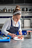 Woman in apron spooning sweet cream with a spoon while cooking delicious dessert in kitchen of modern restaurant