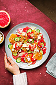 Overhead of crop person eating delicious healthy salad with strawberry and orange and cucumber slices with cheese and pistachios on plate