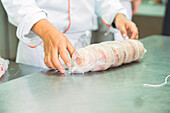 Crop anonymous cooks in uniforms and aprons rolling raw meat in clingfilm while cooking together