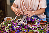Crop anonymous female florist creating wreath from fresh colorful flowers while working at table in shop
